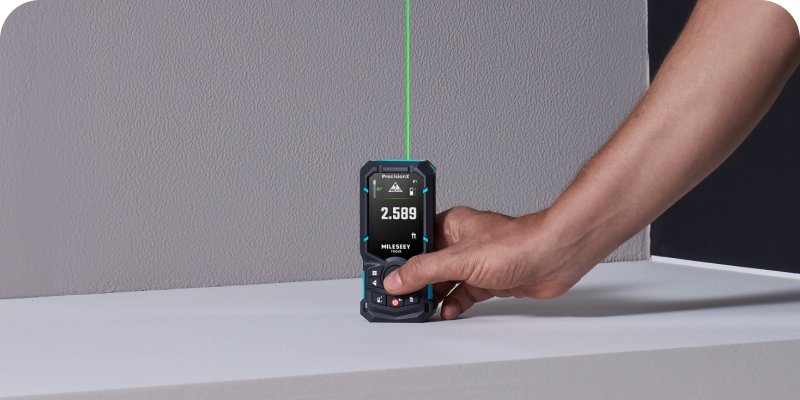 MILESEEY S50 laser distance meter measuring wall height with a green laser beam