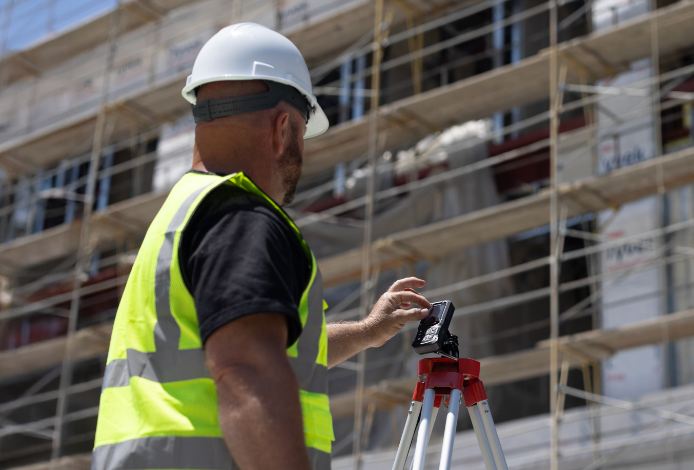Construction professional using a tripod-mounted laser distance measure outside a building